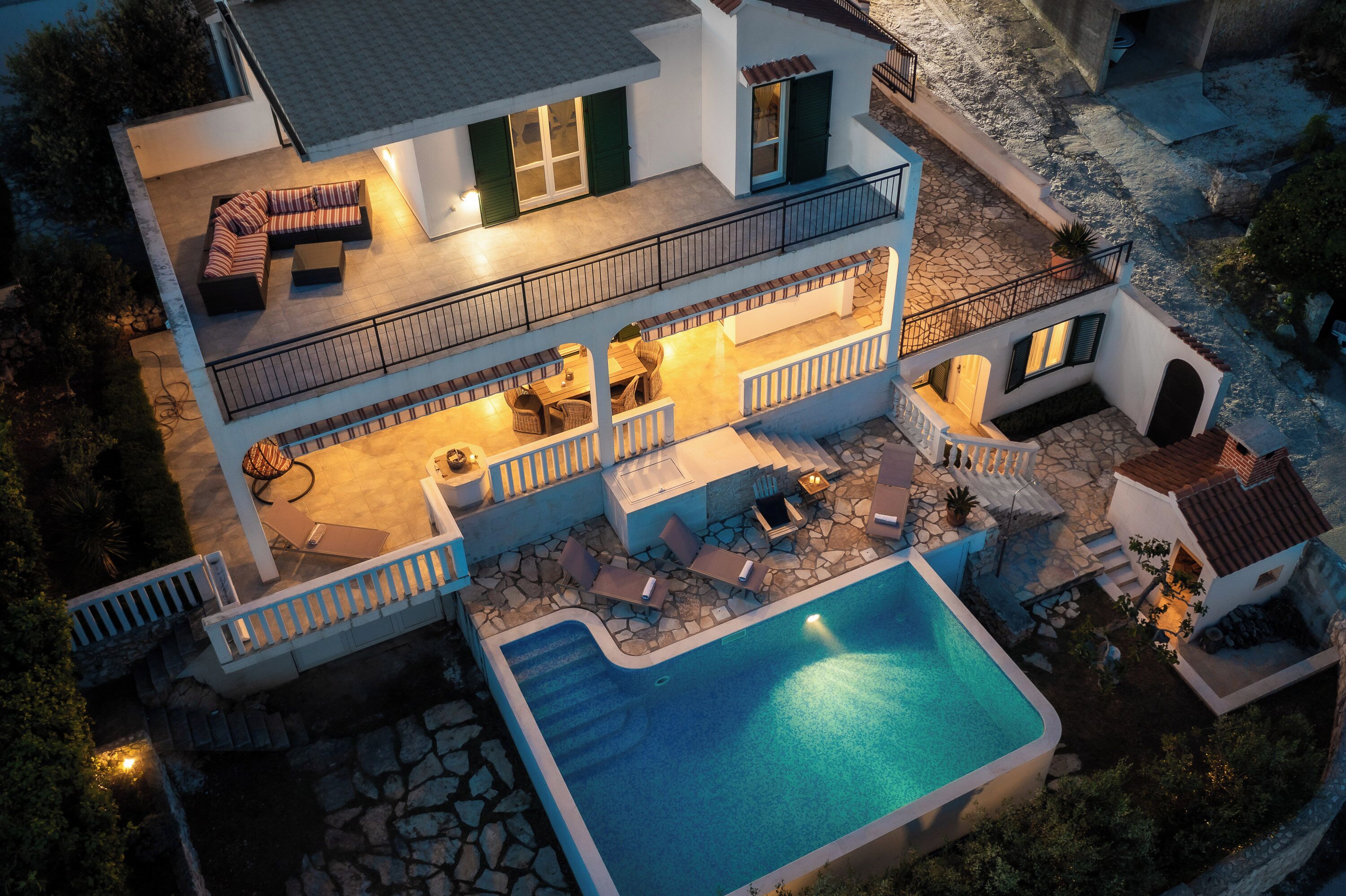 Una casa de dos pisos con piscina, mobiliario exterior y un balcón.