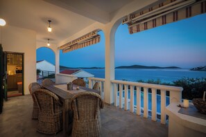 Eine Terrasse mit Korbmöbeln, Blick auf das Meer und einem weißen Geländer.