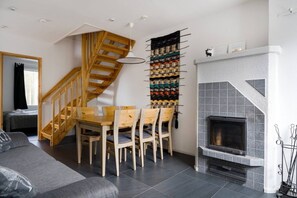 Un espacio habitable moderno con una escalera de madera, una zona de comedor con mesa y sillas, una chimenea y una pared decorada con un tapiz colorido.