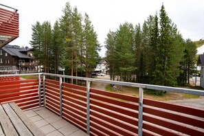 Een balkon met een metalen hekwerk, met uitzicht op een parkeerplaats en een rij bomen.