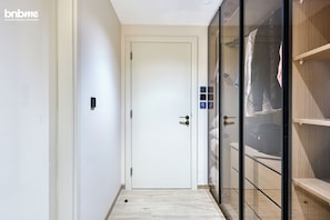 A hotel corridor with a white door, a glass partition, and a wooden shelf unit.