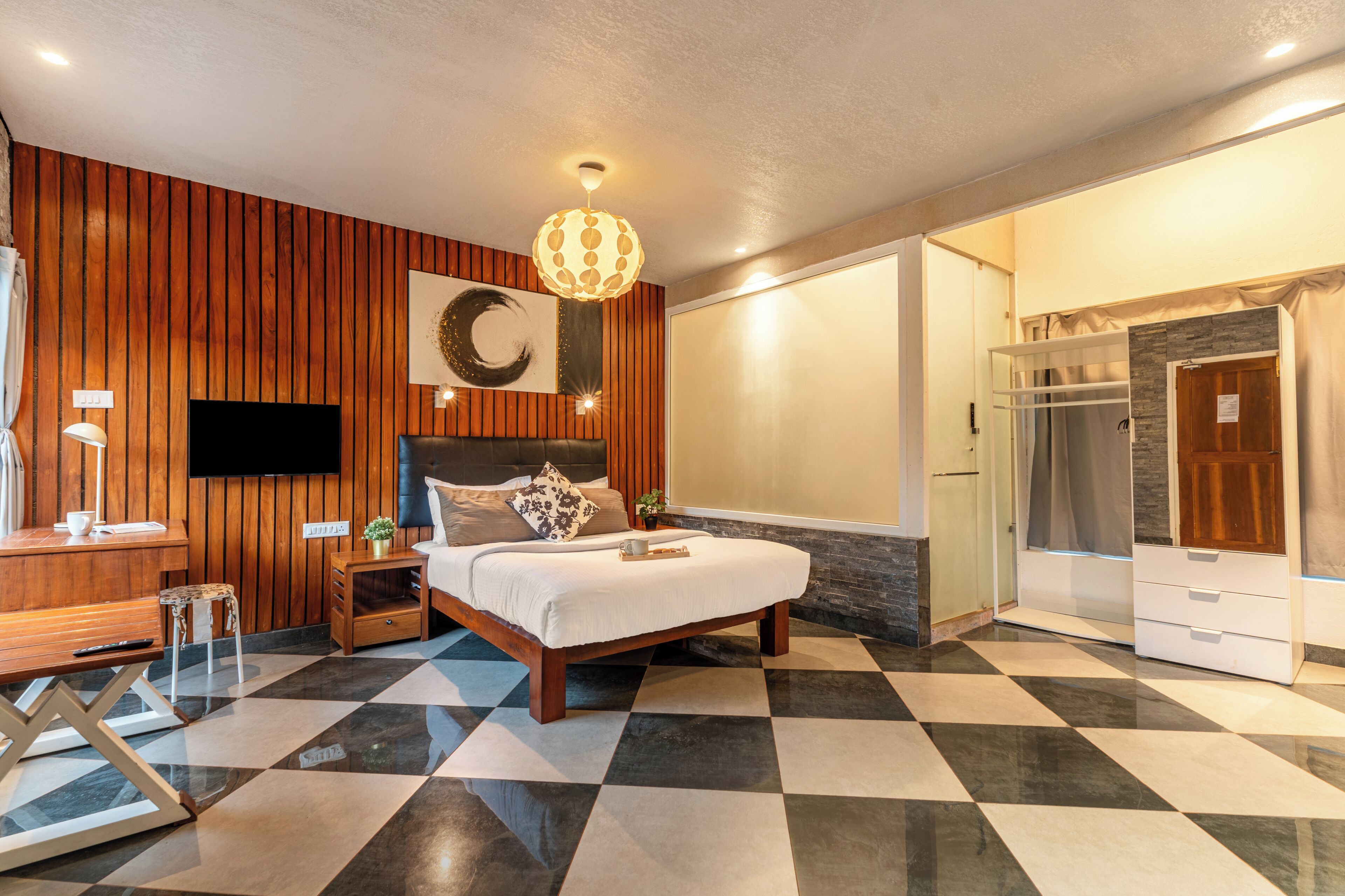 A modern bedroom with a checkered floor, a bed with a headboard, a mounted TV, and a shower area.
