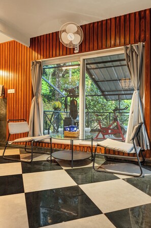 A room with a checkered floor, two chairs, a fan, and a window with curtains.