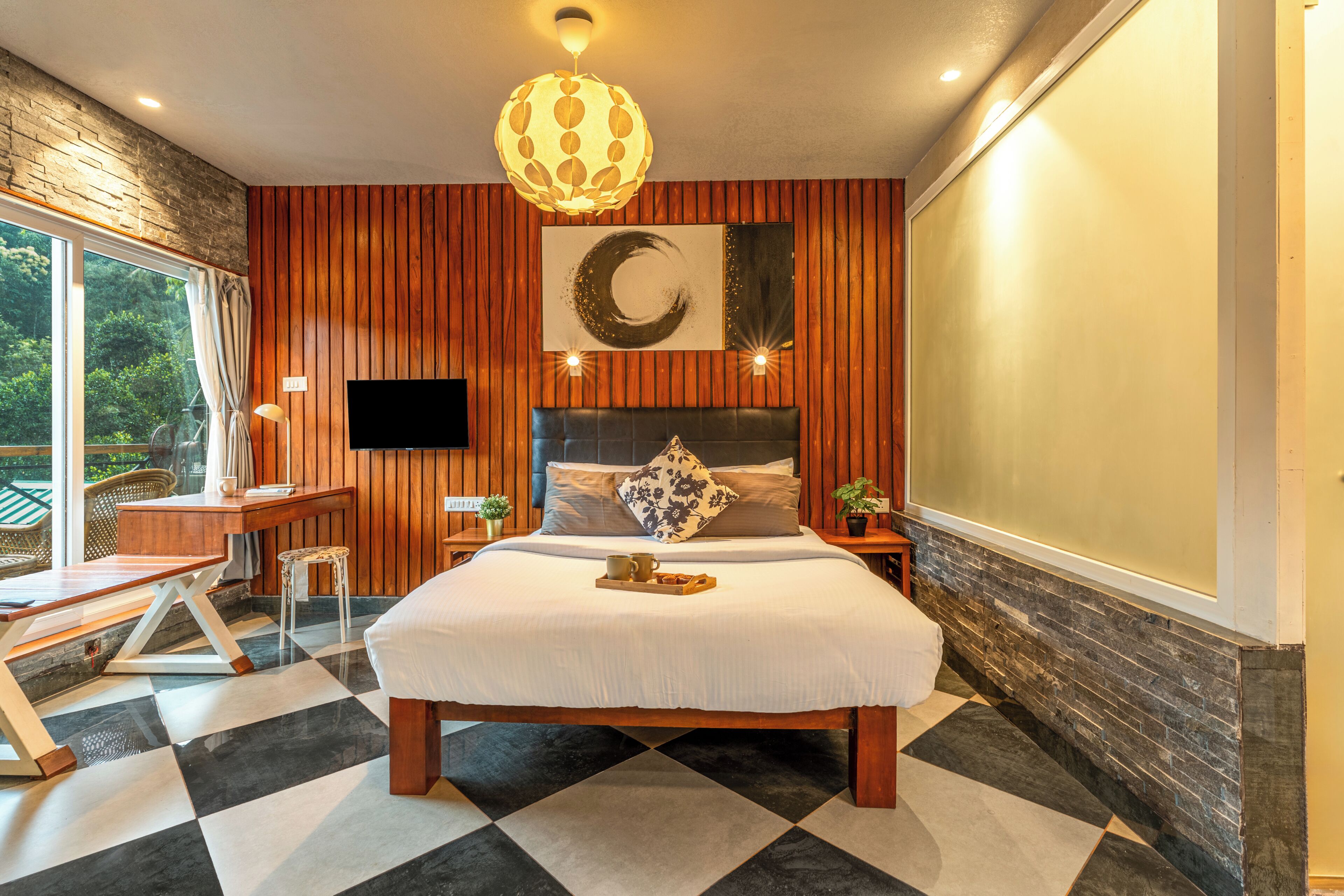 A modern hotel room with a large bed, wooden panel walls, a mounted TV, and a view of the outdoors.