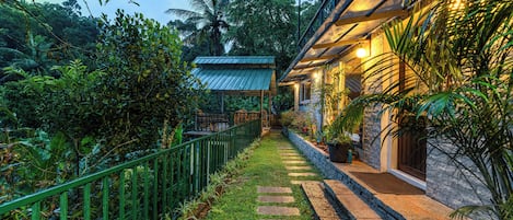 A pathway leading to a building with a stone facade and a metal roof.