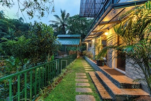 A pathway leading to a building with a stone facade and a metal roof.