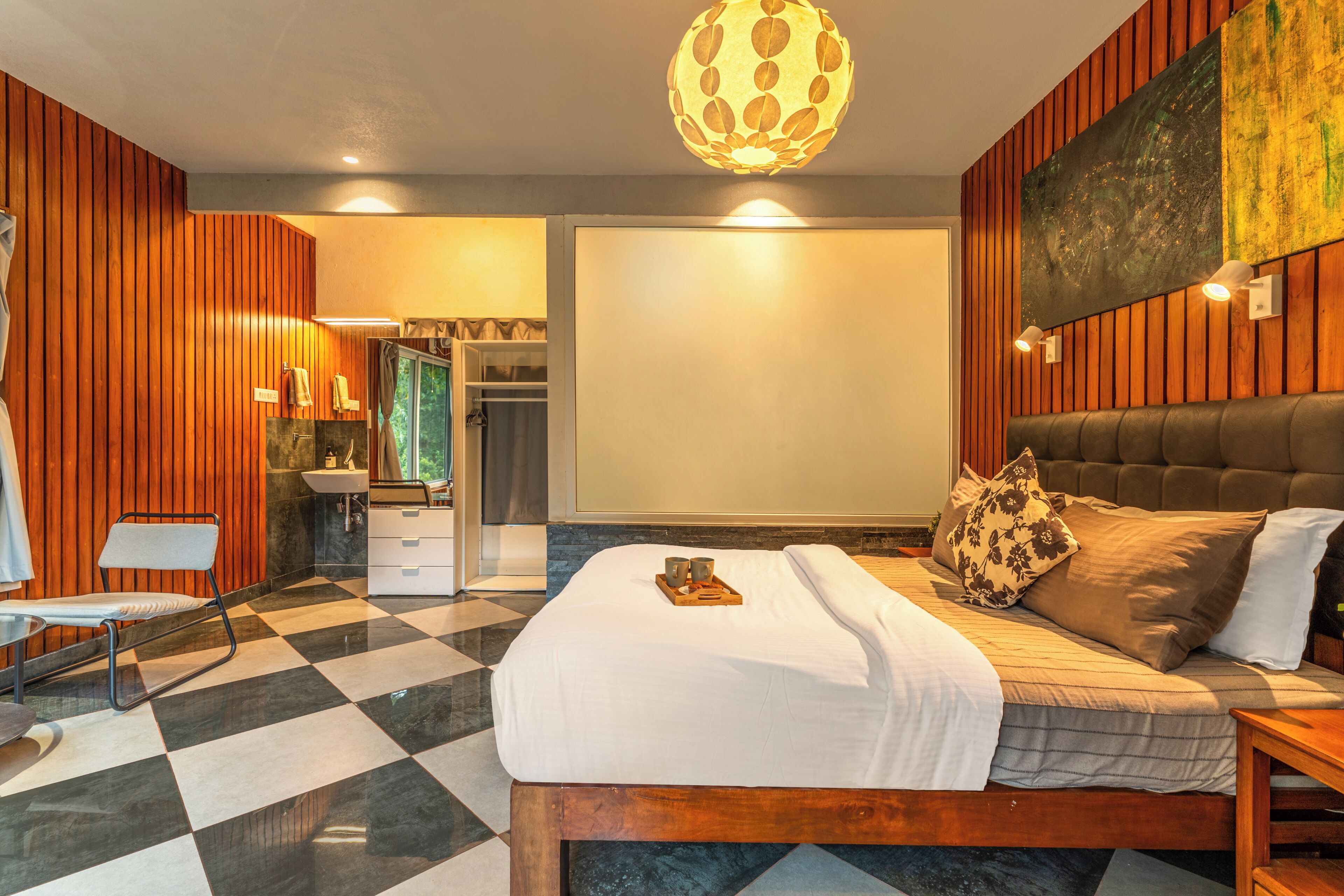 Una habitación de hotel con piso a cuadros, una cama con una bandeja de objetos, un cabecero de madera y un cuadro grande en la pared.