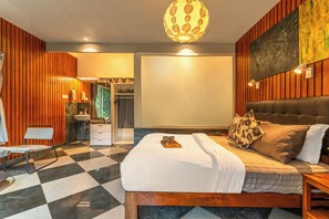 Una habitación de hotel con piso a cuadros, una cama con una bandeja de objetos, un cabecero de madera y un cuadro grande en la pared.