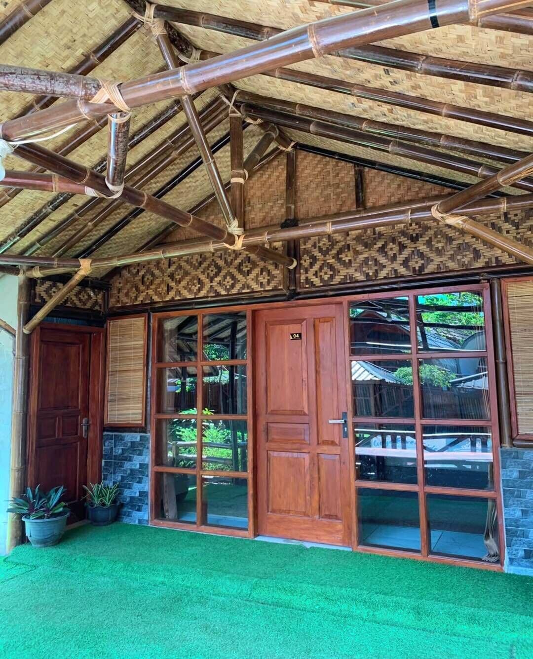 Un bâtiment de style traditionnel, doté d’un toit en bambou, de grandes portes en bois et d’une pelouse artificielle verte.