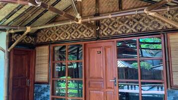 Un bâtiment de style traditionnel, doté d’un toit en bambou, de grandes portes en bois et d’une pelouse artificielle verte.