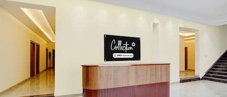 A reception desk with a sign above it, a staircase to the right, and a hallway with doors on the left.