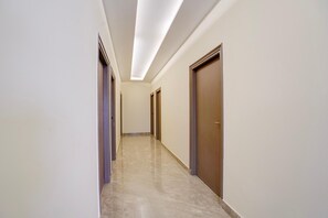 Un couloir avec des portes de part et d’autre, un sol carrelé et un plafond doté d’un éclairage encastré.