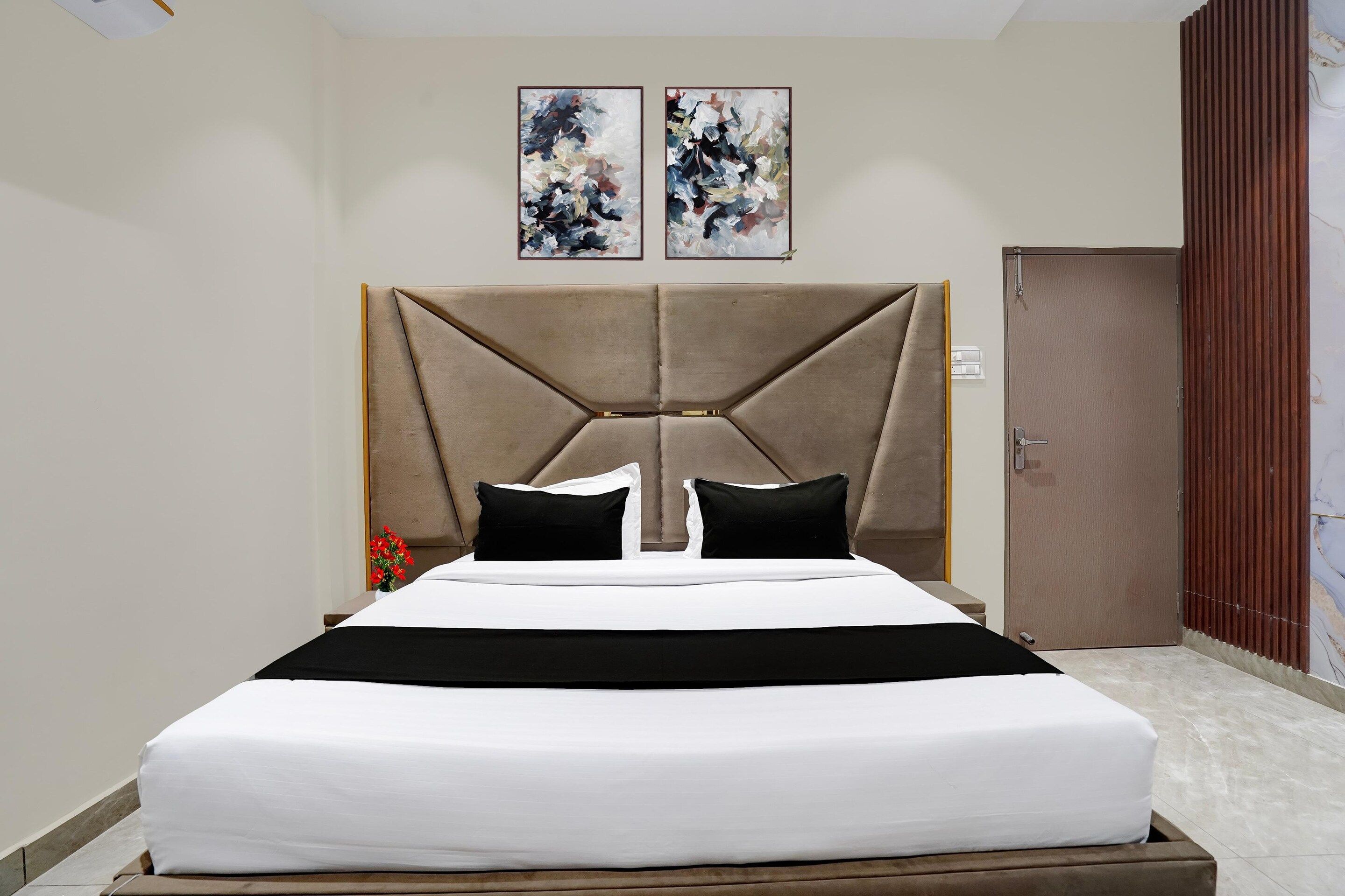 A hotel room with a bed, a headboard, two paintings, and a door.