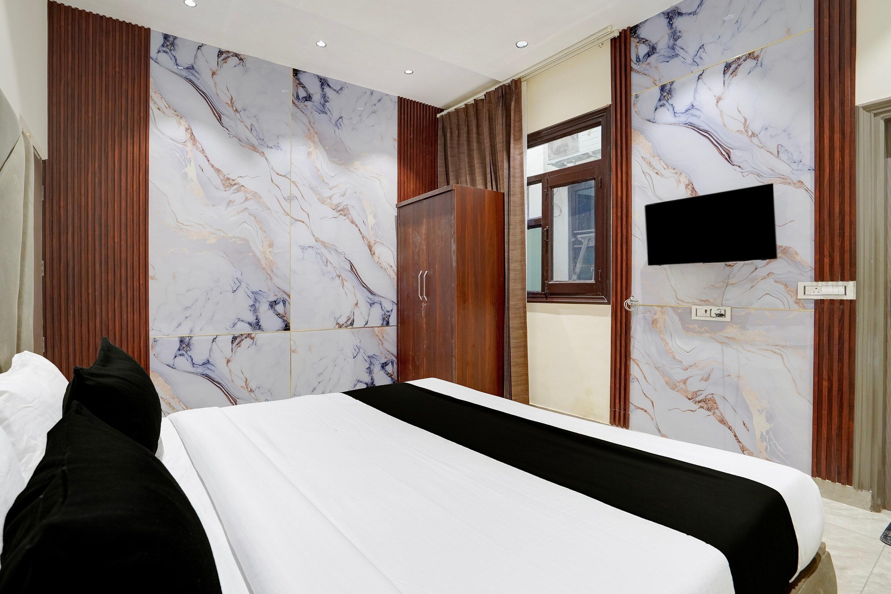 A hotel room with a bed, wooden wardrobe, a television, and marble-patterned walls.