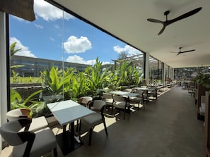 An indoor dining area with tables and chairs, large windows, and ceiling fans. - Niyara - Contemporary African Hotel (Arusha)