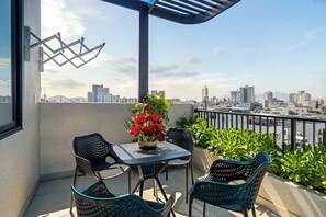 Uma varanda com mesa e cadeiras, um vaso com flores vermelhas e vista para a cidade.
