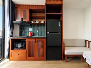 A compact kitchen with a black refrigerator, wooden cabinets, a microwave, and a red kettle. - Sola House Apartment (Da Nang)