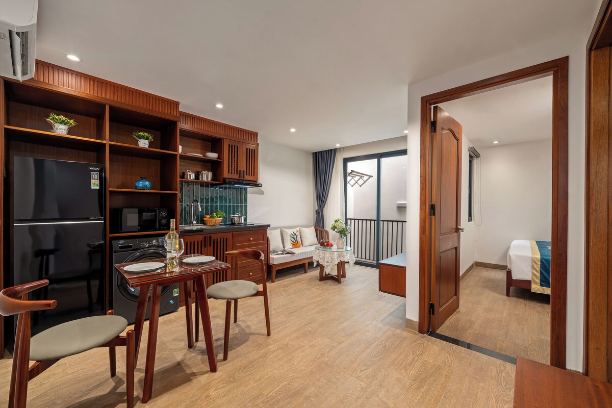 Cozinha moderna com armários de madeira, mesa de jantar com cadeiras e sala de estar com sofá e varanda.