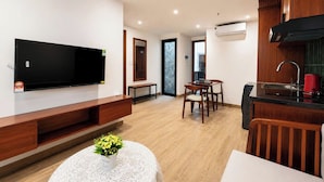 Una sala de estar moderna con televisor de pantalla plana, muebles de madera, un comedor y una cocina con extractor de aire negro.