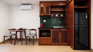 Cocina compacta con muebles de madera, un refrigerador negro, un microondas y un comedor con dos sillas y una mesa.