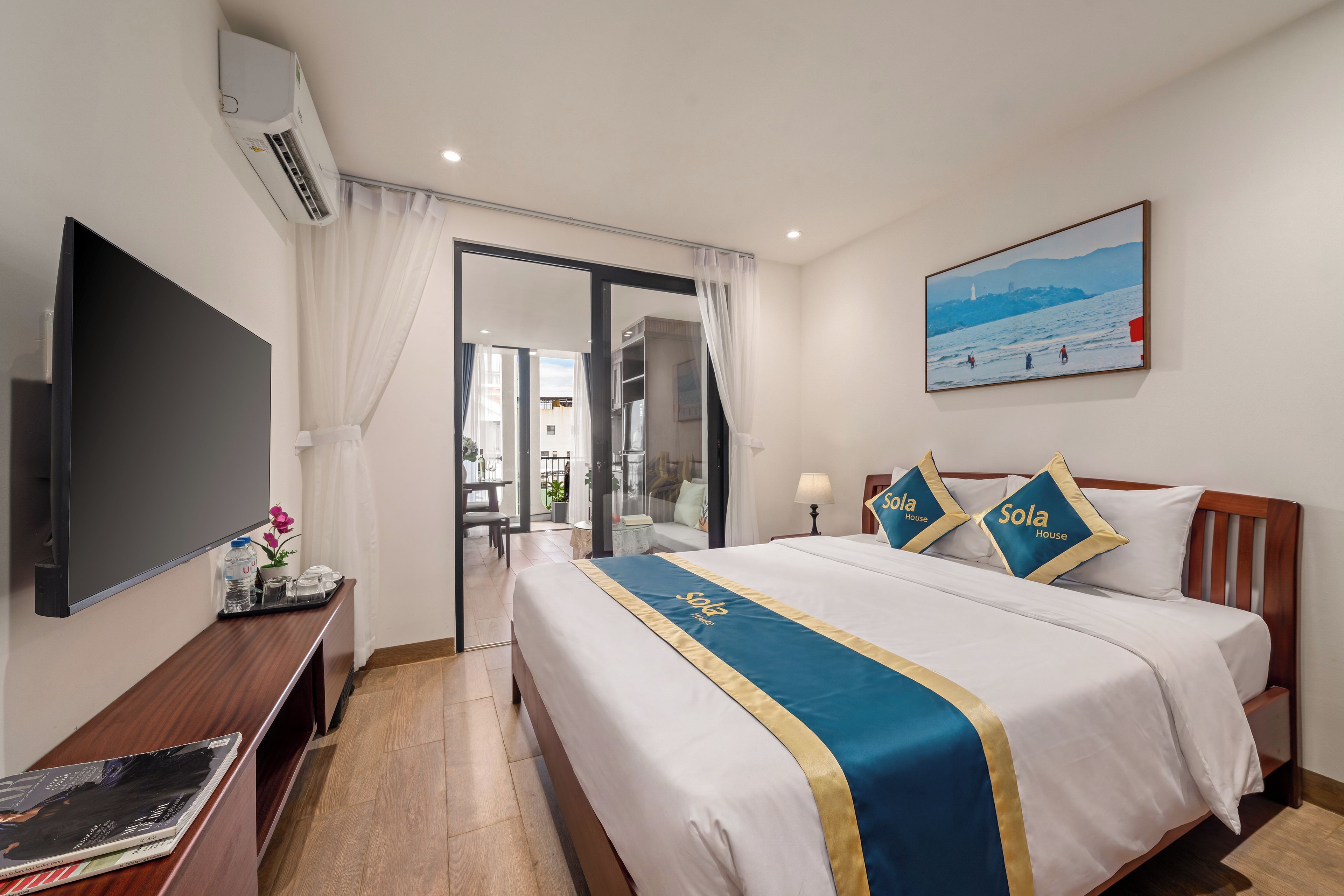 Quarto de hotel com cama, televisão, escrivaninha e um quadro na parede.