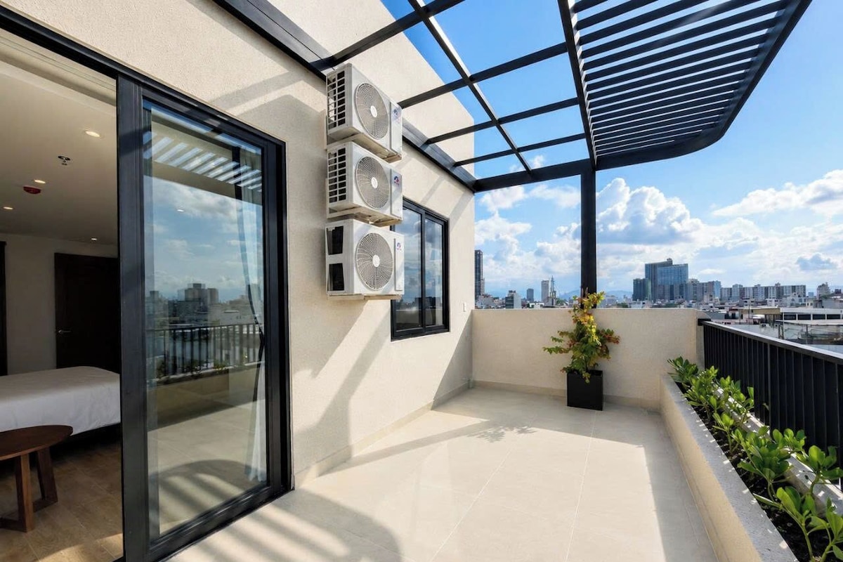 Un balcon avec une porte-fenêtre donnant sur une pièce, des unités de climatisation, une plante en pot et une vue sur la ville.