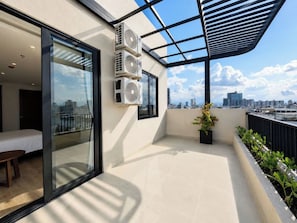 Un balcon avec une porte-fenêtre donnant sur une pièce, des unités de climatisation, une plante en pot et une vue sur la ville.