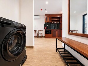 A laundry area with a front-loading washer and dryer, a wooden bench, and a kitchen area with wooden cabinets and a countertop. - Sola House Apartment (Da Nang)