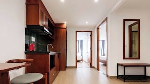 Una cocina moderna con armarios de madera, un comedor con mesa y sillas, y un pasillo que lleva a un dormitorio.