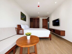 Habitación de hotel con cama, sofá, mesa de madera con planta, televisor y armario.