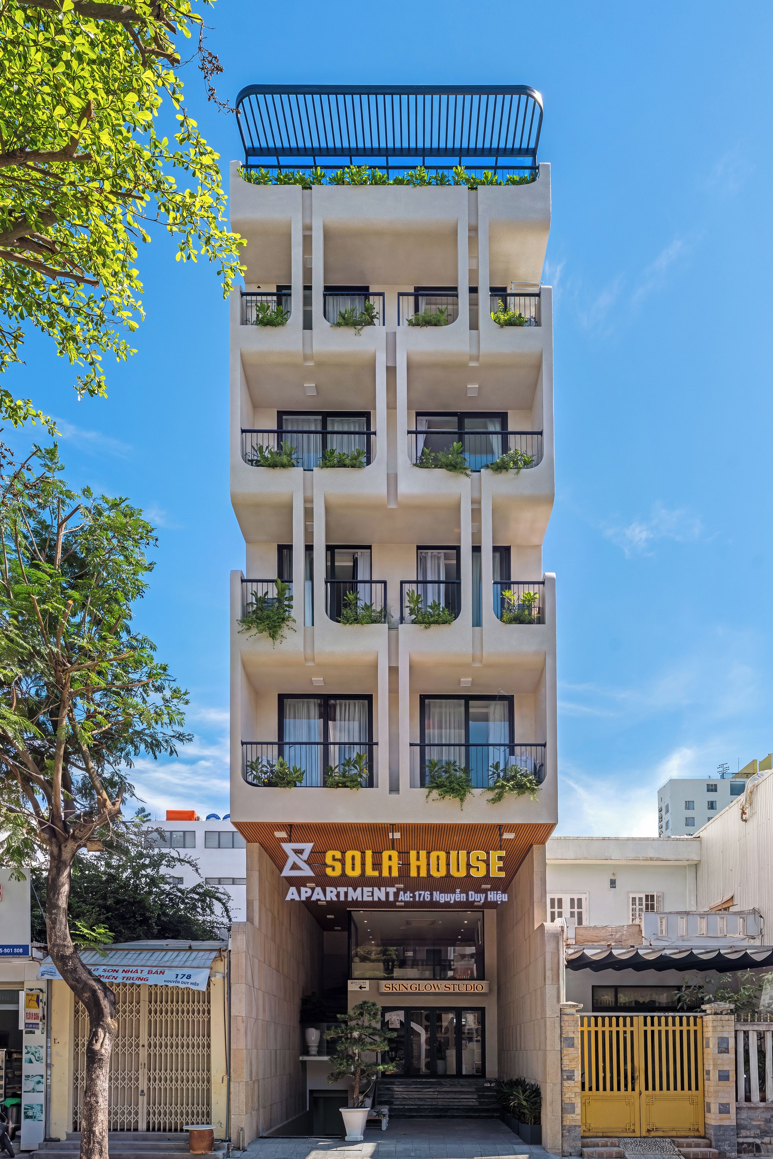 Un edificio de varios pisos con balcones, un letrero que dice 'Sola House Apartment' y una tienda con el rótulo 'Skin Glow Studio'.