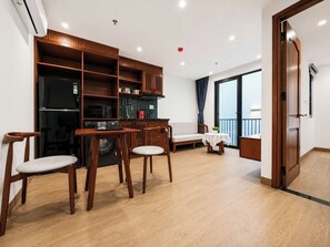 A modern living room with a dining area, wooden furniture, a built-in kitchen, and a large window. - Sola House Apartment (Da Nang)