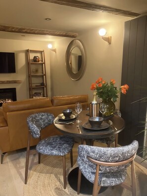 A dining area with a round table, chairs, a vase with flowers, and a television mounted on the wall. - Ullswater retreat near Helvellyn-Bath & EV charger (Glenridding)