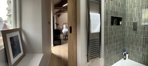 A bathroom with a tiled wall, a towel hanging on a rack, and a framed picture on the floor. - Ullswater retreat near Helvellyn-Bath & EV charger (Glenridding)