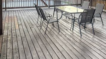 A covered wooden deck with a table and chairs, a view of a backyard, and a wooden fence.