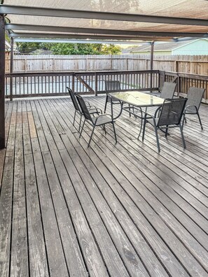 A covered wooden deck with a table and chairs, a view of a backyard, and a wooden fence. - Eddy (Pasadena)