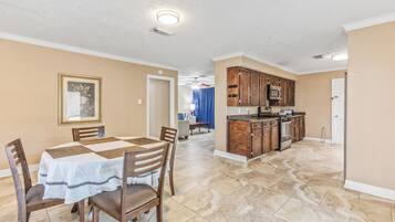 A dining area with a table and chairs, a kitchen with wooden cabinets and appliances, and a hallway with a door.