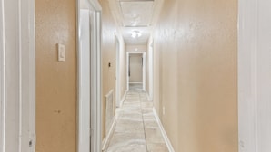 A hallway with a tiled floor, white walls, and a door on the left. - Eddy (Pasadena)