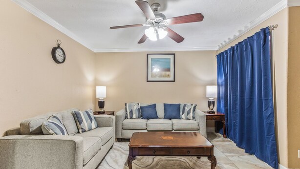 A living room with a ceiling fan, two sofas, a coffee table, and a large window with blue curtains. - Eddy (Pasadena)