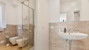 Un bagno moderno con cabina doccia in vetro, lavandino bianco con articoli da toilette e water.