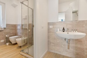 Ein modernes Badezimmer mit einer Duschkabine, einem weißen Waschbecken mit Pflegeprodukten und einer Toilette.