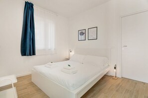Ein Schlafzimmer mit Bett, Nachttischen, einem Fenster mit Vorhängen und einer Tür.