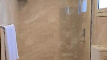 A bathroom with a glass-enclosed shower, a toilet, and a marble floor.