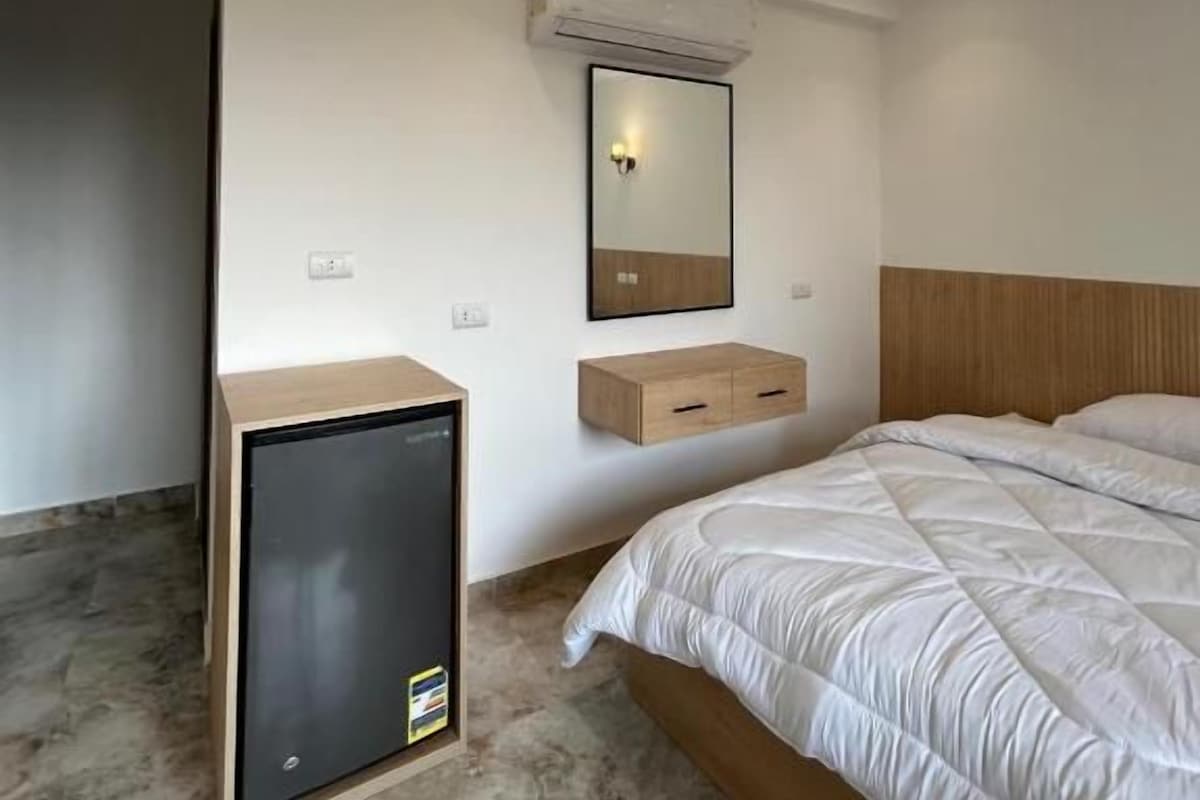 A bedroom with a bed, bedside table, mirror, and a small cabinet.