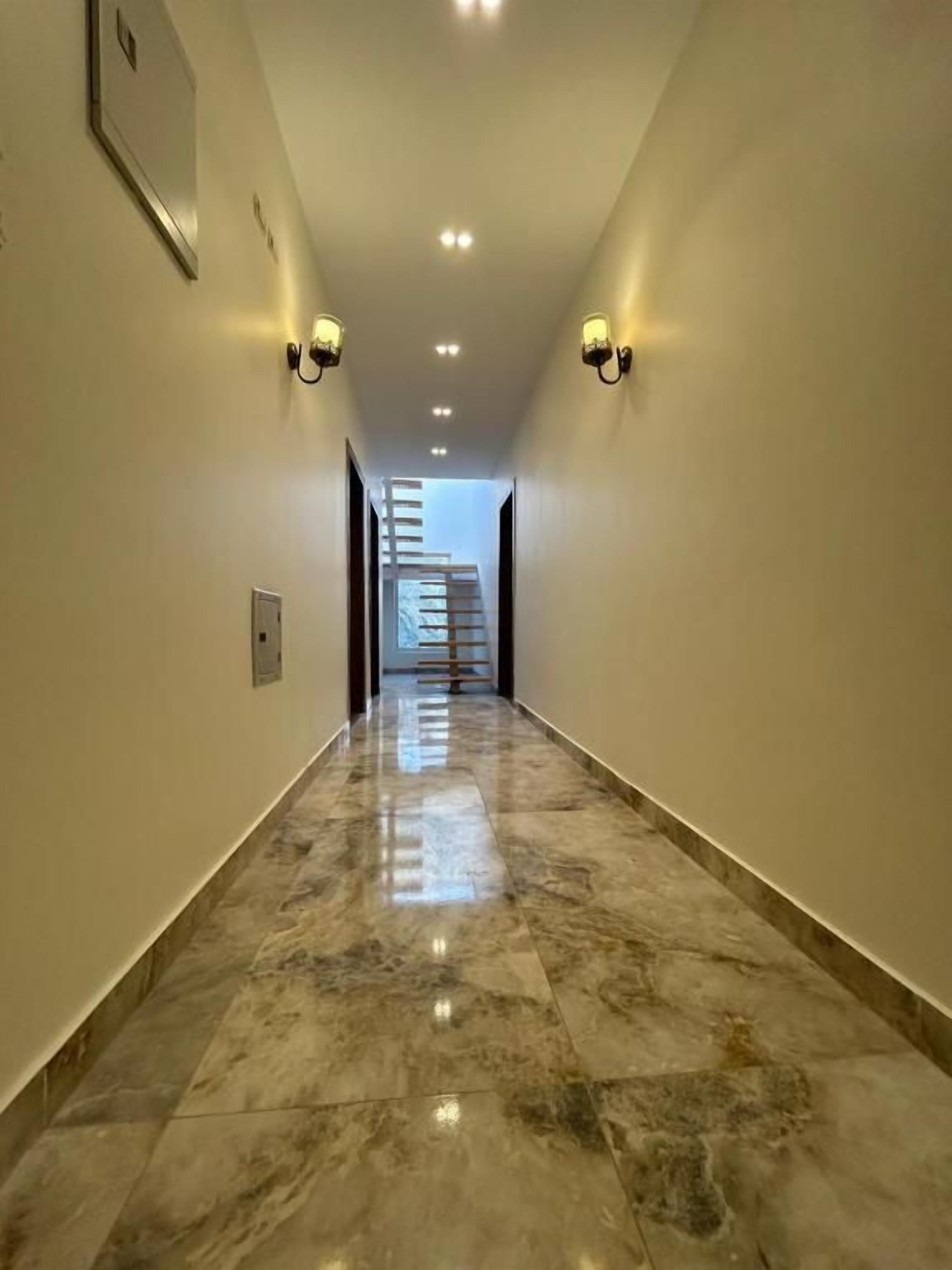 A corridor with marble flooring, wall-mounted sconces, and a staircase in the distance.