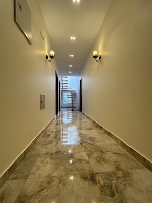 Un pasillo con piso de mármol, apliques de pared y una escalera al fondo.