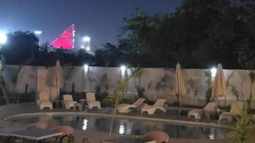 A poolside area with lounge chairs and umbrellas, surrounded by a low wall and trees.