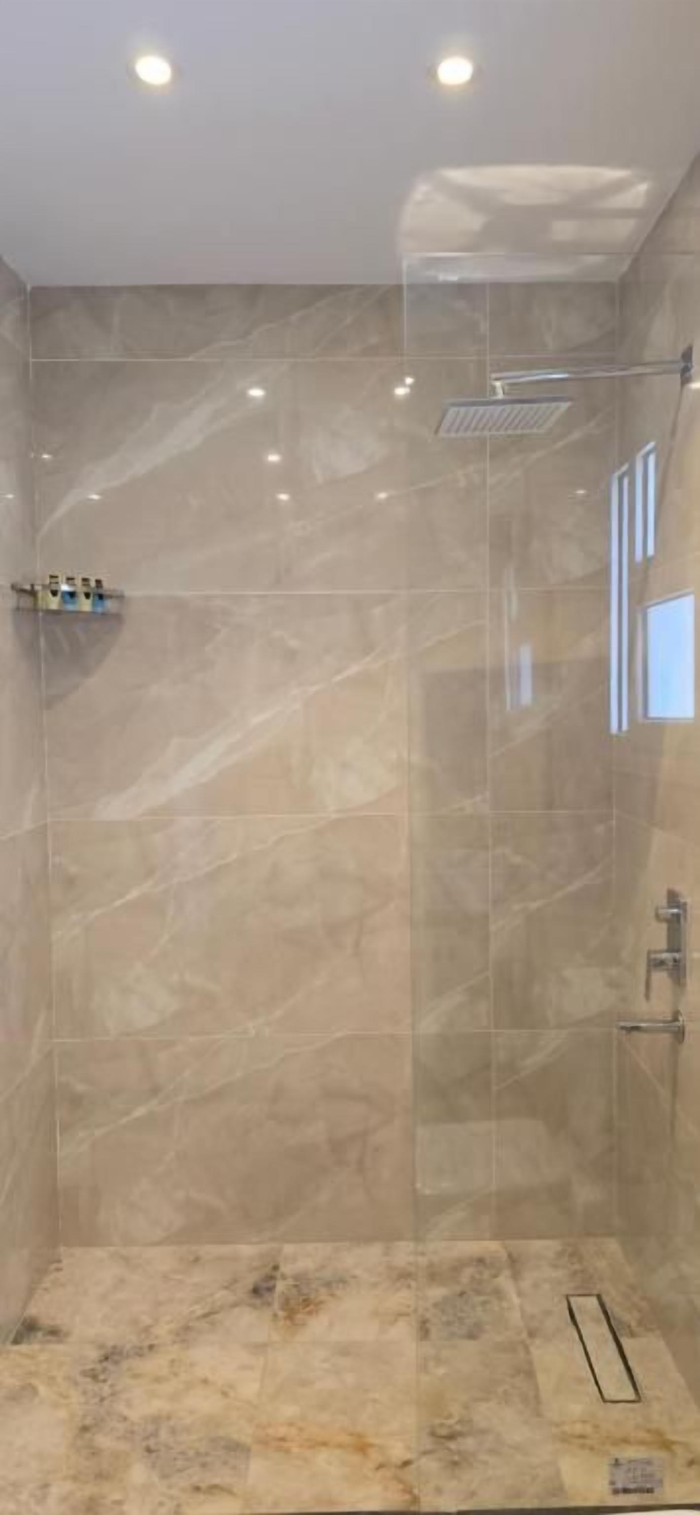 A glass-enclosed shower with a marble floor and a ceiling light fixture.