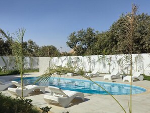 Una piscina con sillas de descanso, rodeada de follaje y un cielo despejado.