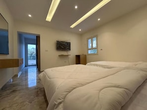 Un dormitorio moderno con una cama grande, un televisor de pantalla plana montado en la pared y un ventanal que proporciona luz natural.